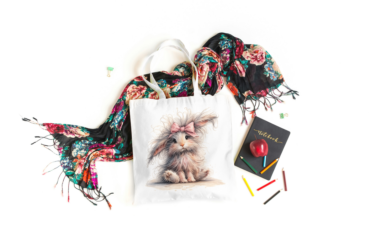 Tote bag with a cat print, floral scarf, notebook, and pencils on a white background